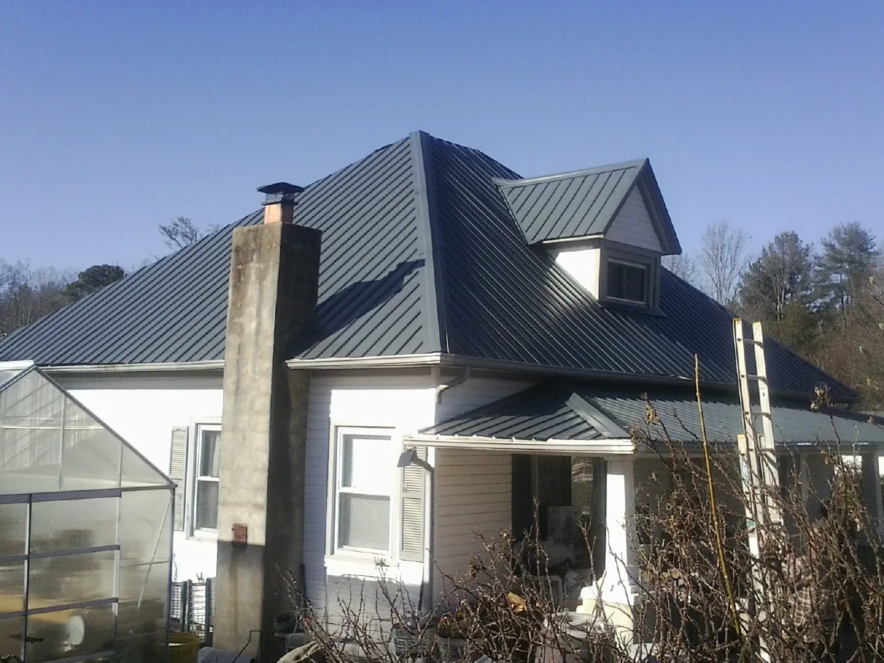 Dark blue standing seam metal roof on a white farmhouse with dormer in Ritzville