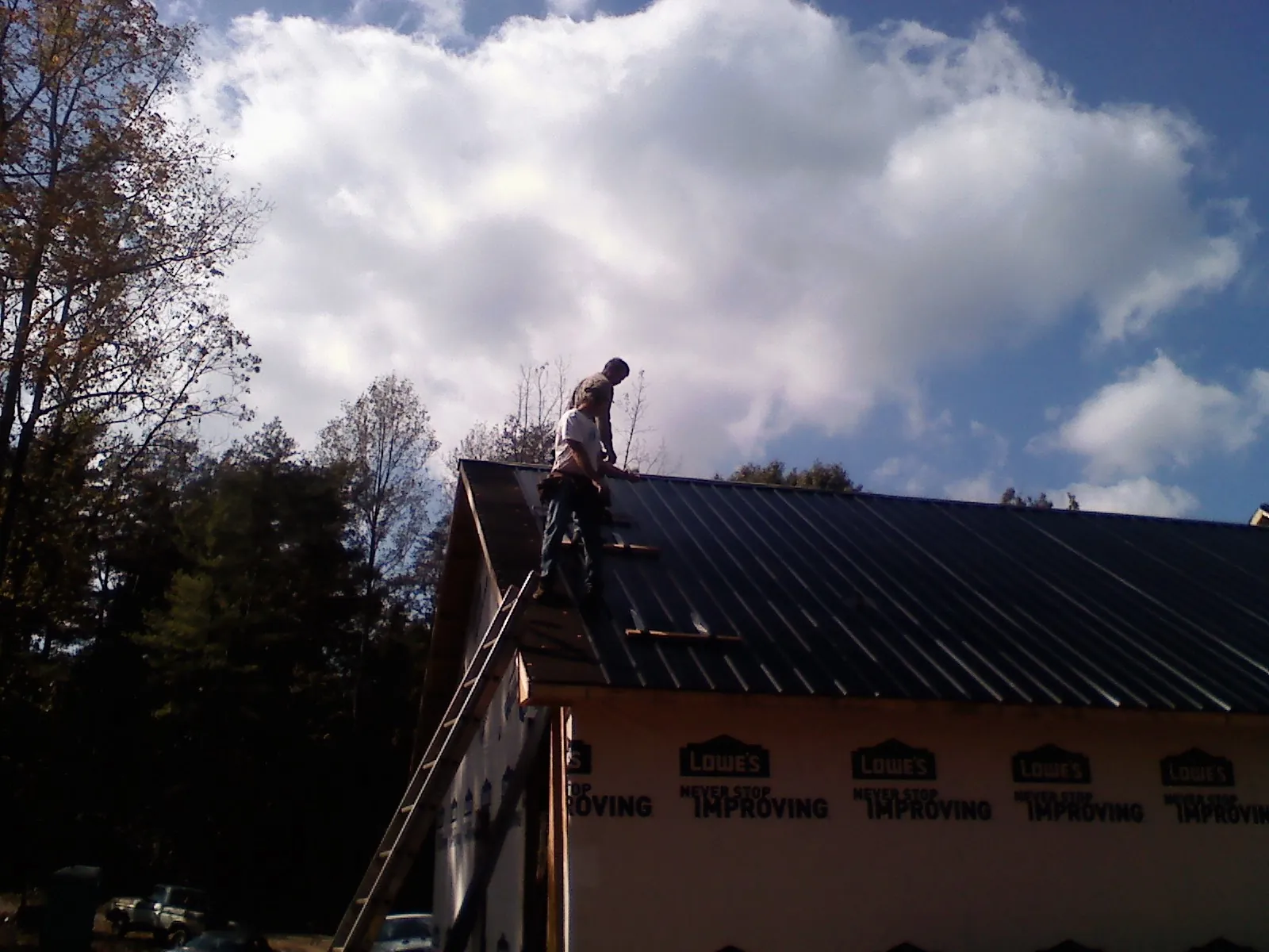 Roofer fastening dark metal panels high against a cloudy sky, from a Roof Inspection job in Ritzville